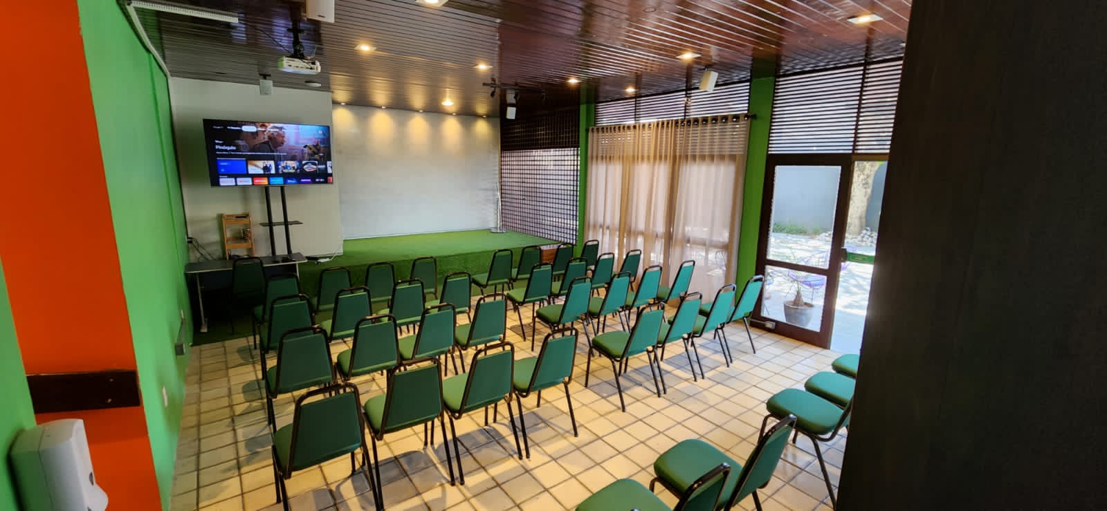 Auditório vazio, montado em plenária, com o palco e a porta de vidro que dá para o pátio
