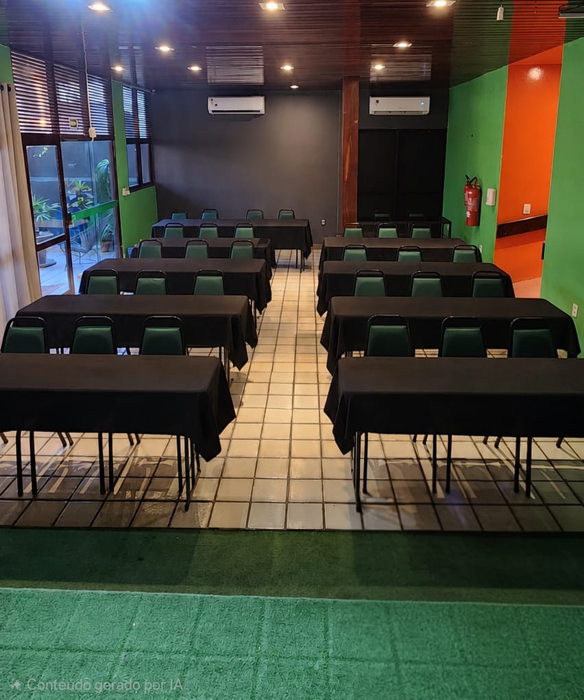 Auditório montado em formato escolar, com mesas vestidas de preto em fileiras e cadeiras voltadas para a frente