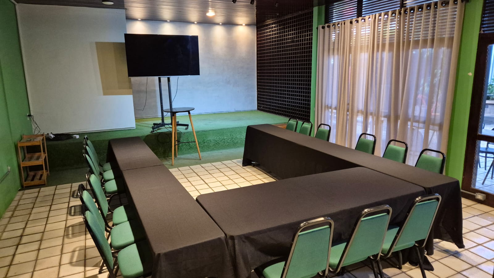 Auditório montado em formato U, com mesas vestidas de preto voltadas para a TV e o palco